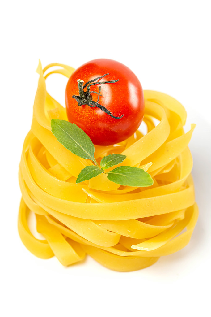 Raw tagliatelle pasta with tomato and basil, close up