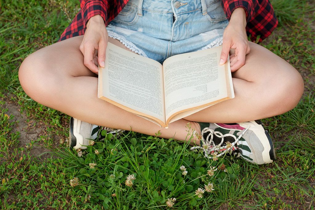 Reading a book in nature, a girl sits on the grass and reads a book