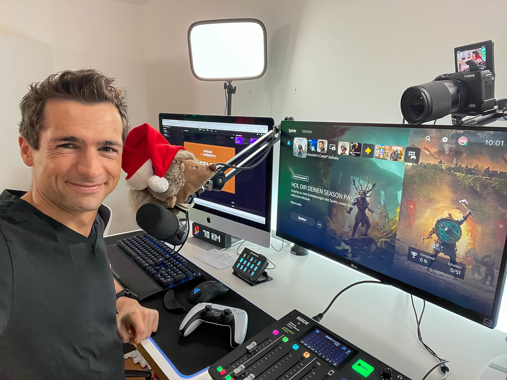 Ready for streaming: smiling in front of the camera at the desk with two screens, microphone, controller