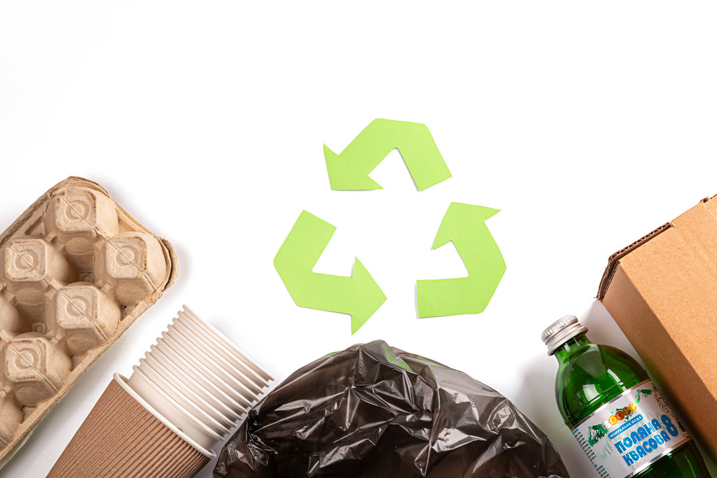 Recycle concept, green arrows icon among waste on white background, top view