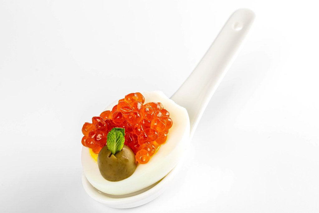Red caviar canape with egg and olive in white spoon