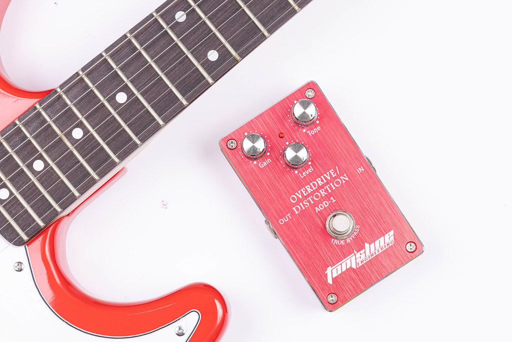 Red Distortion pedal and electric Guitar above white background