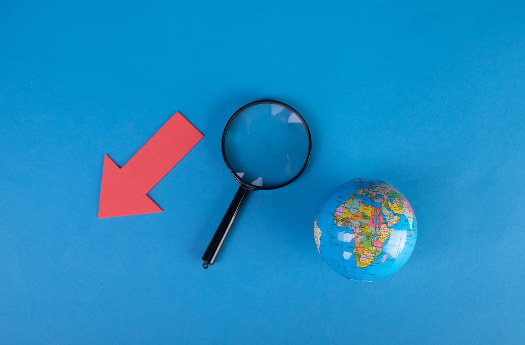 Red down arrow with magnifying glass and globe on blue background