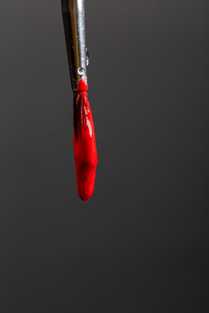 Red paint drips down a brush on a black background