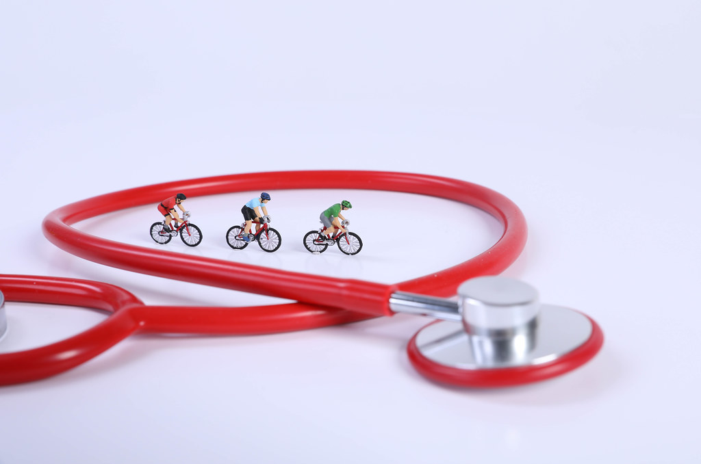 Red stethoscope and miniature cyclists on white background