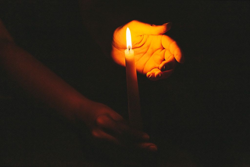 Religious concept, hands holding a burning candle on dark background