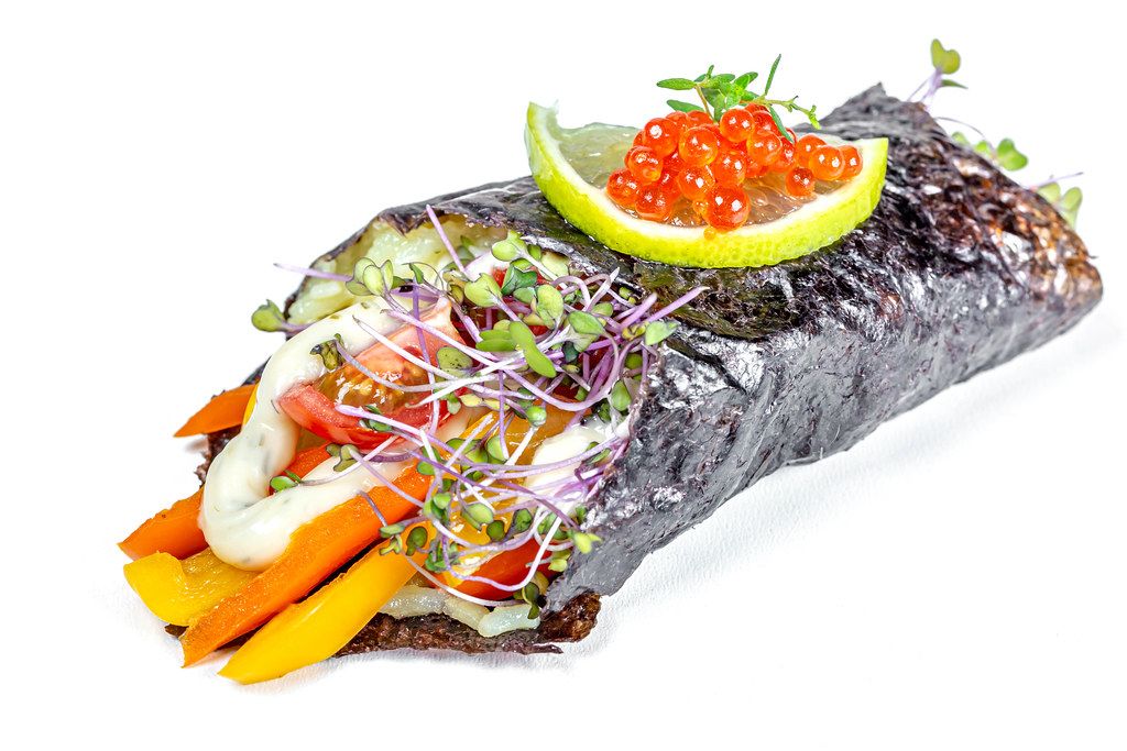 Rice, vegetables, sauce and microgreens wrapped in nori with red caviar and lime