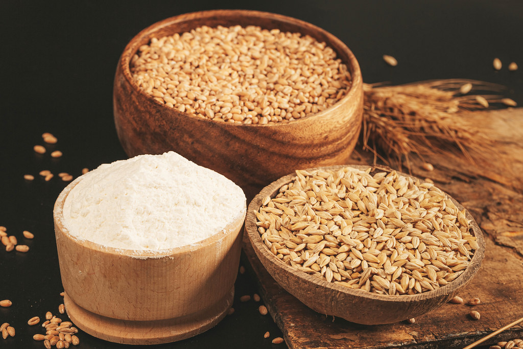 Ripe wheat, barley and flour in wooden bowls