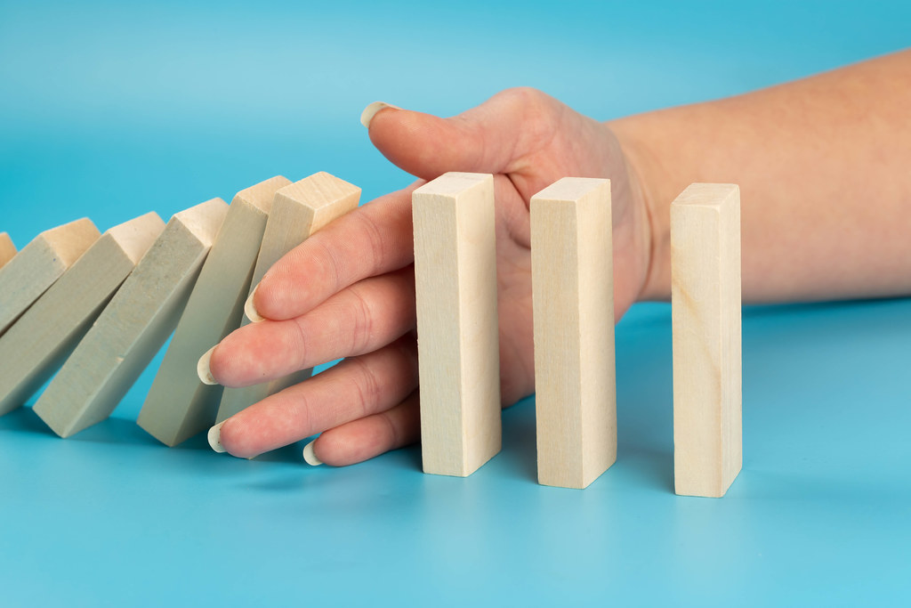 Risk and strategy in business, close up of hand stopping wooden block from falling in the line of domino