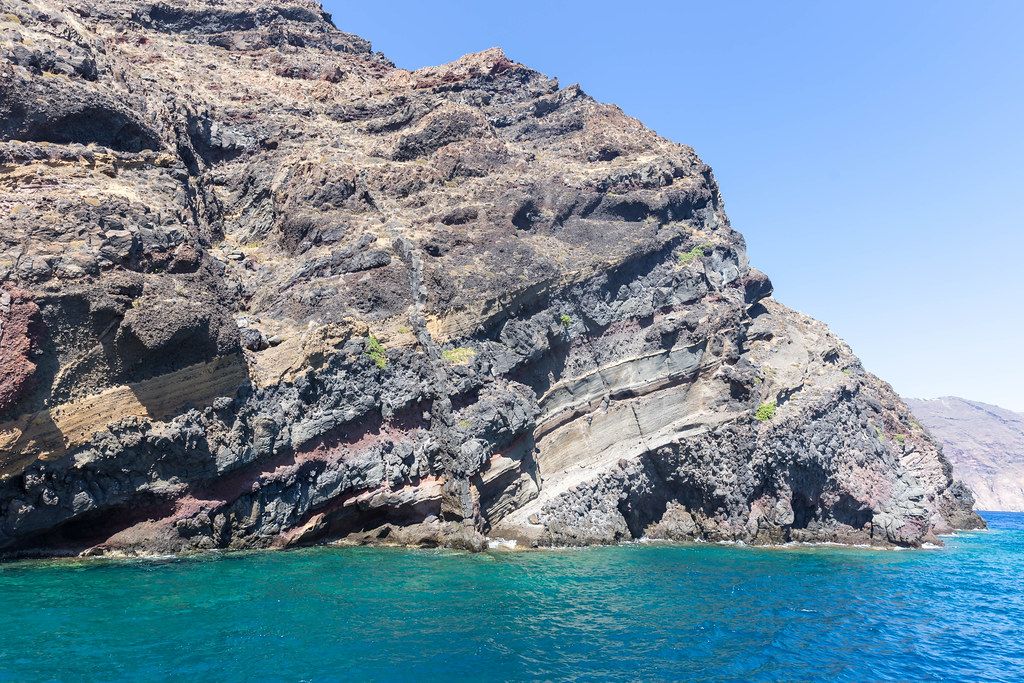 Rock layers and crystal clear waters: the steep cliffs of Santorini and the Aegean Sea during a boat trip