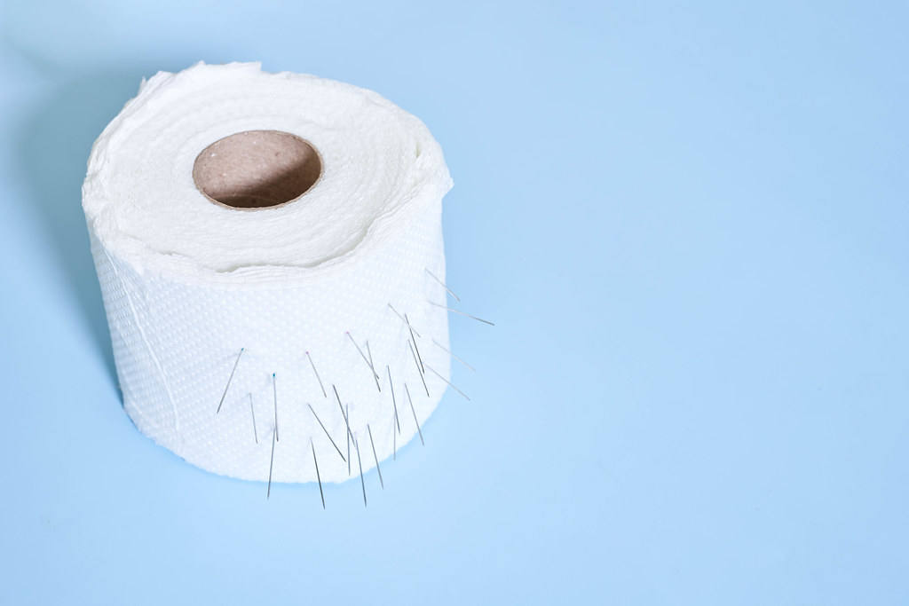 Roll of toilet paper with nails on blue background - Hemorrhoid problems