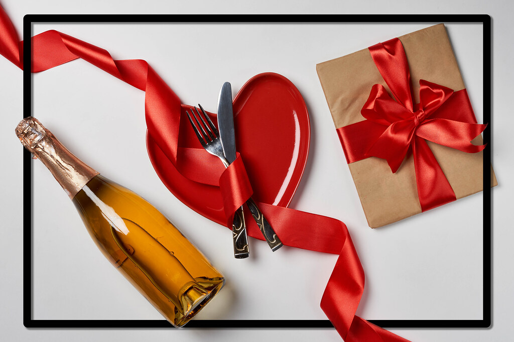 Romantic love background with gift, champagne bottle and red plate with ribbon.