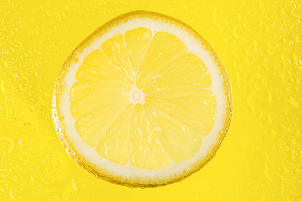 Round lemon slice on yellow background with water drops