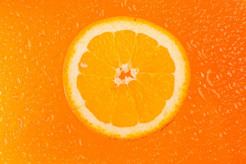 Round orange slice with water drops on orange background