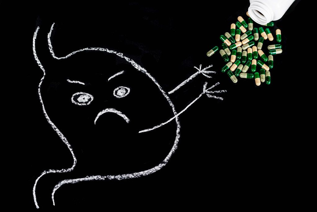 Sad stomach drawn in white chalk on a black background with capsules. Disease concept, bloating