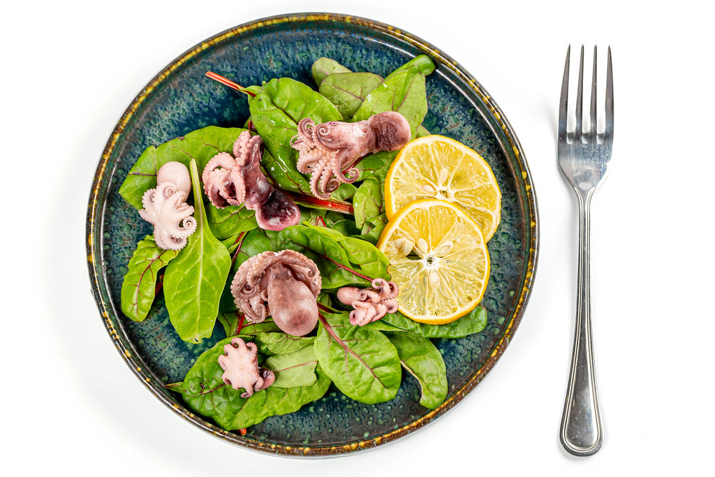 Salad with pickled octopus and green beet leaves on white, top view