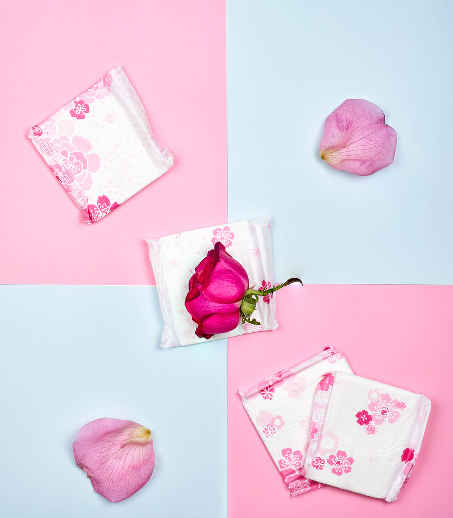 Sanitary pads and flowers on color background