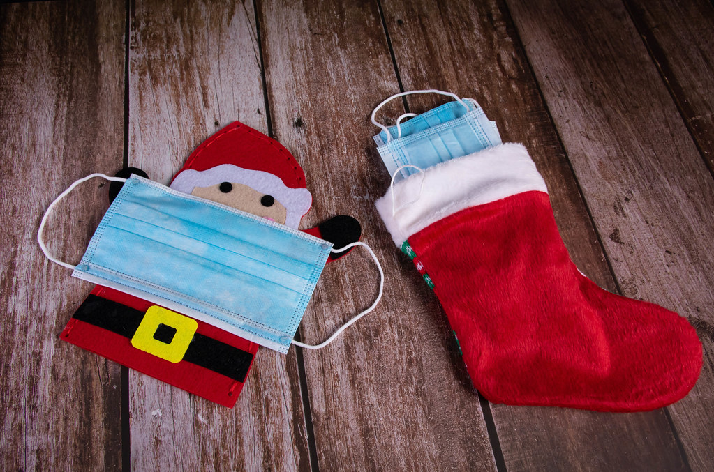 Santa Claus with medical face mask and Christmas sock on wooden background