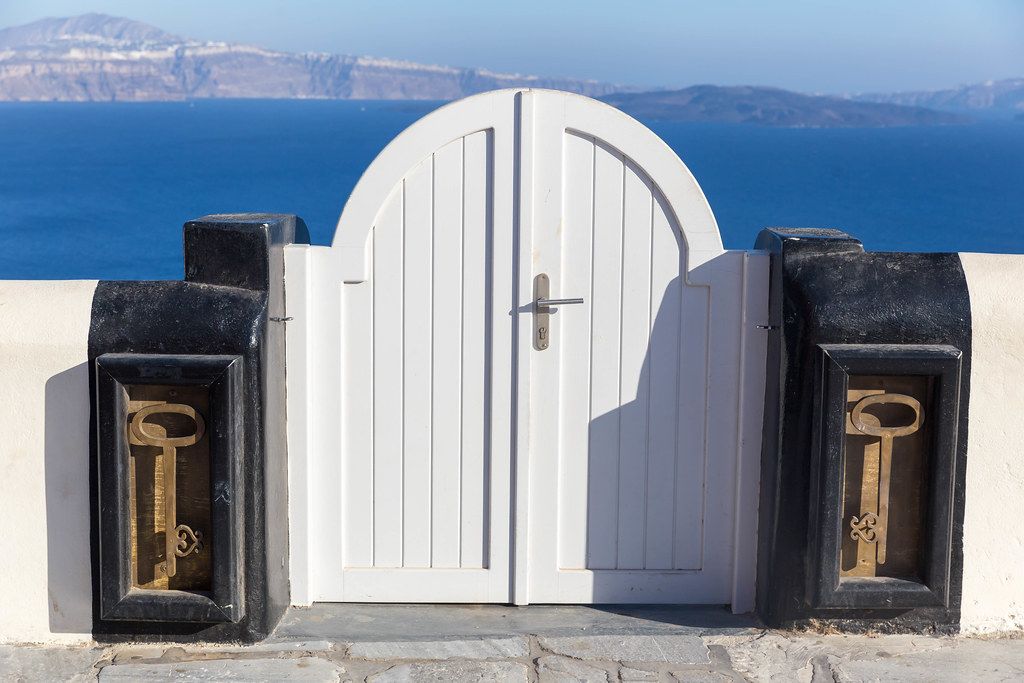 Santorini: closed white gate with a huge key on each side and the sea in the background