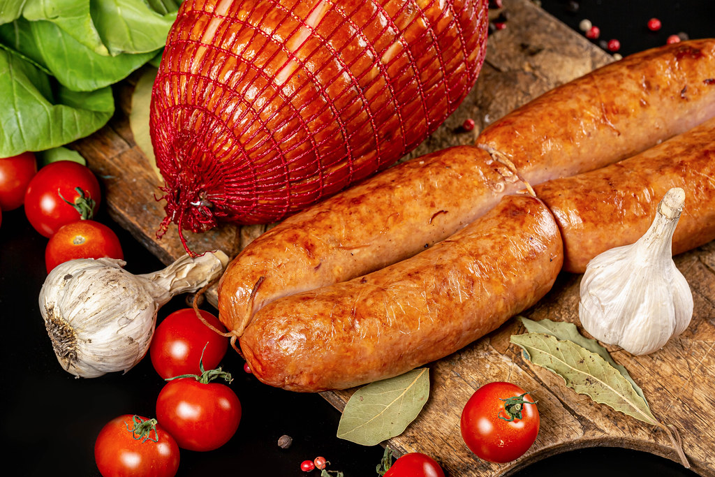 Sausages and ham with spices and tomatoes on a wooden board