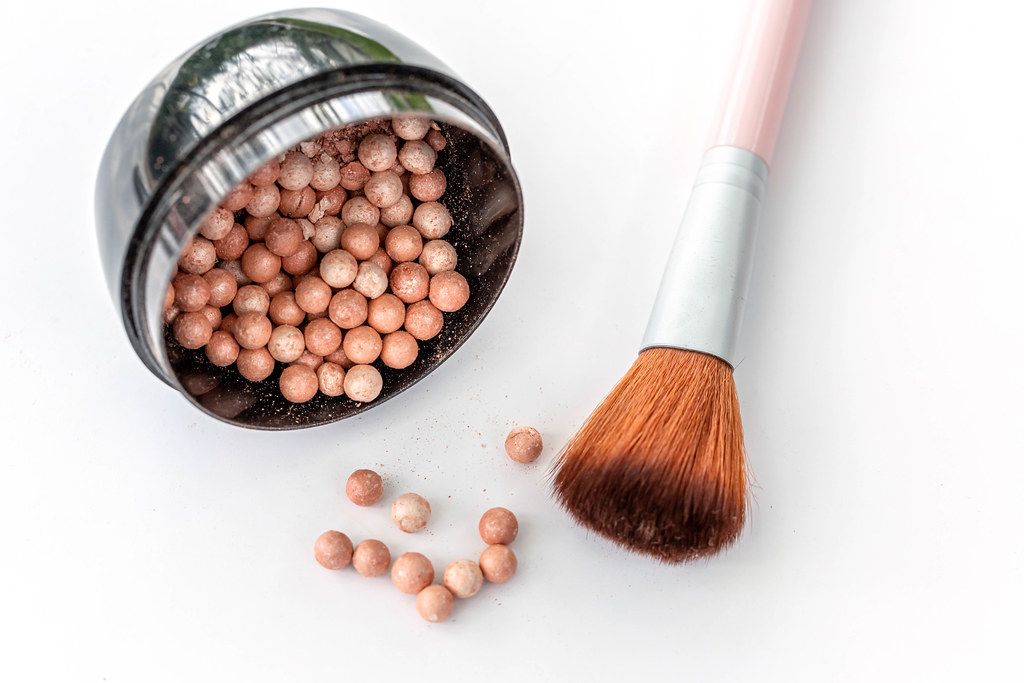 Scattered blush balls on a white background with a brush