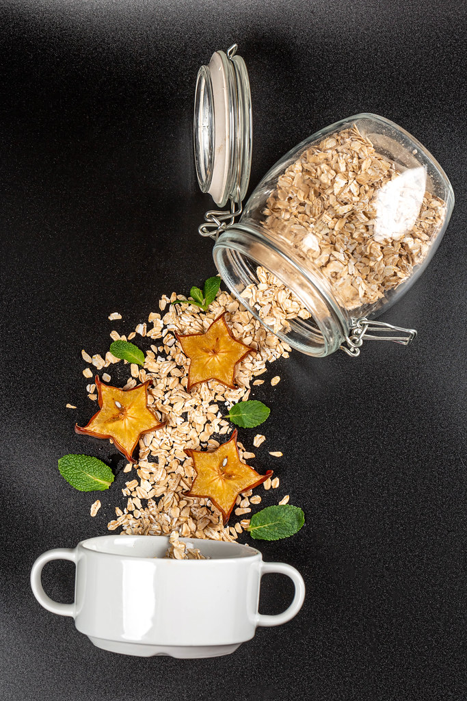 Scattered oatmeal from a jar with slices of carom and mint leaves on a black background and a bowl