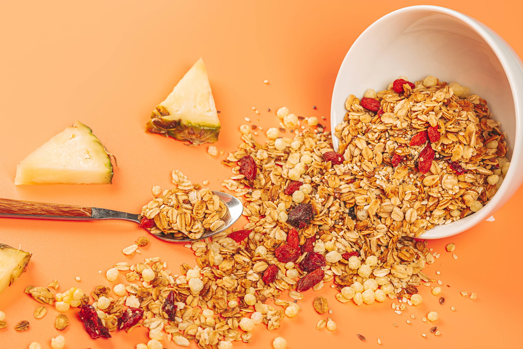 Scattered oatmeal with berries, seeds and pineapple pieces on an orange background