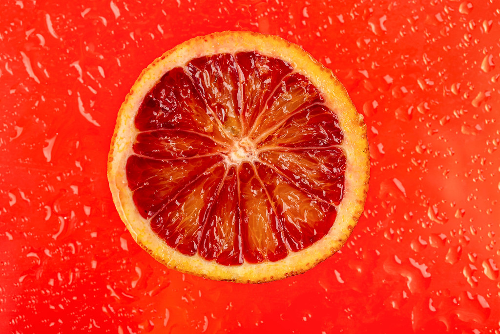 Section of ripe sicilian orange on red background with drops