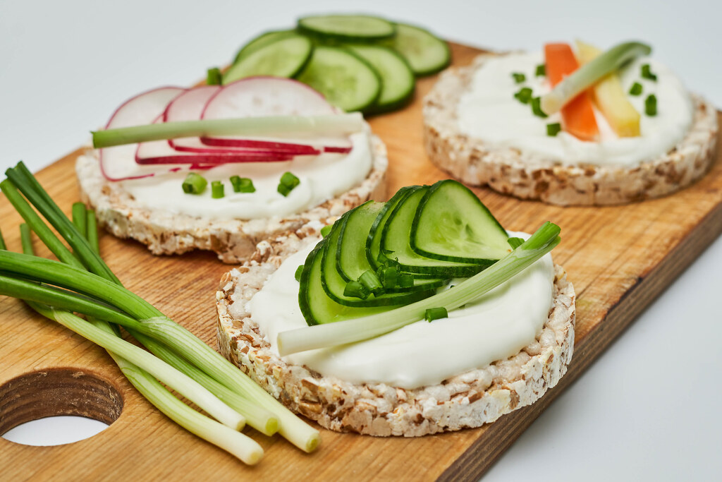 Set of organic sandwiches on dry brown grain crispbreads with fresh vegetables, cream cheese on wooden cutting board