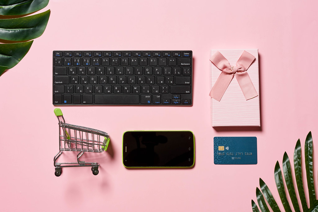 Shopping cart, credit card, mobile phone, gift box and computer keyboard on the pink background