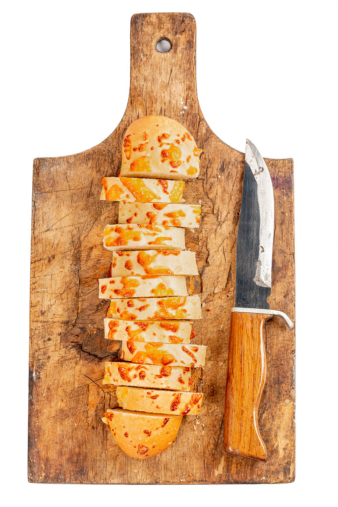 Sliced cheese baguette pieces on an old wooden board with a knife, top view