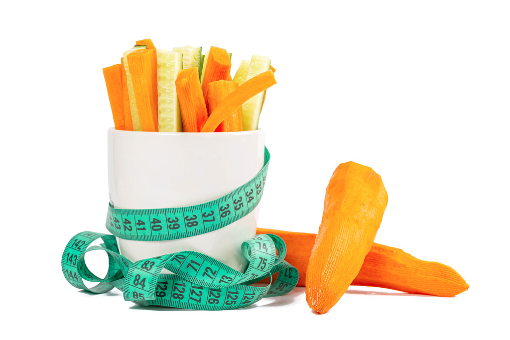 Sliced fresh carrots and cucumbers with a measuring tape on a white background