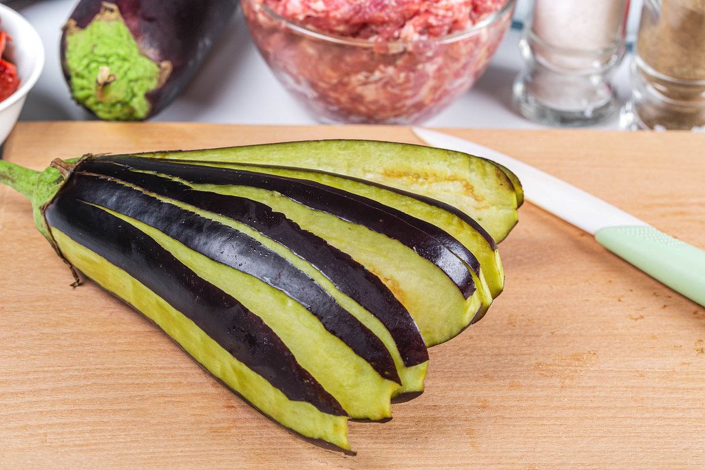 Sliced fresh eggplant on wooden kitchen board and ingredients for filling