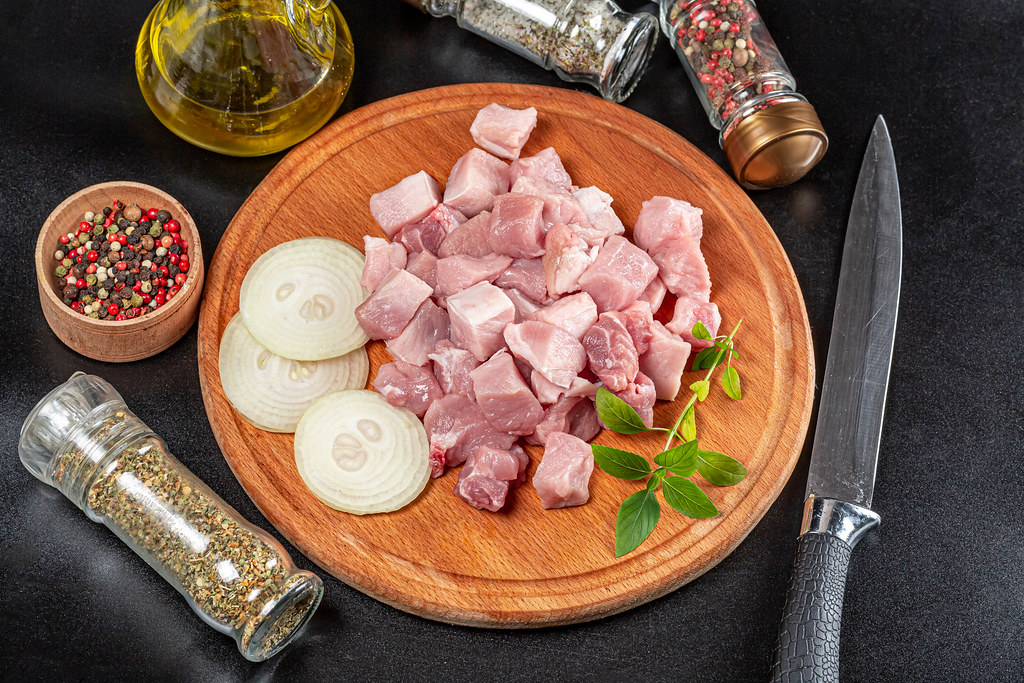 Sliced raw pork meat with spices and a knife on a dark background