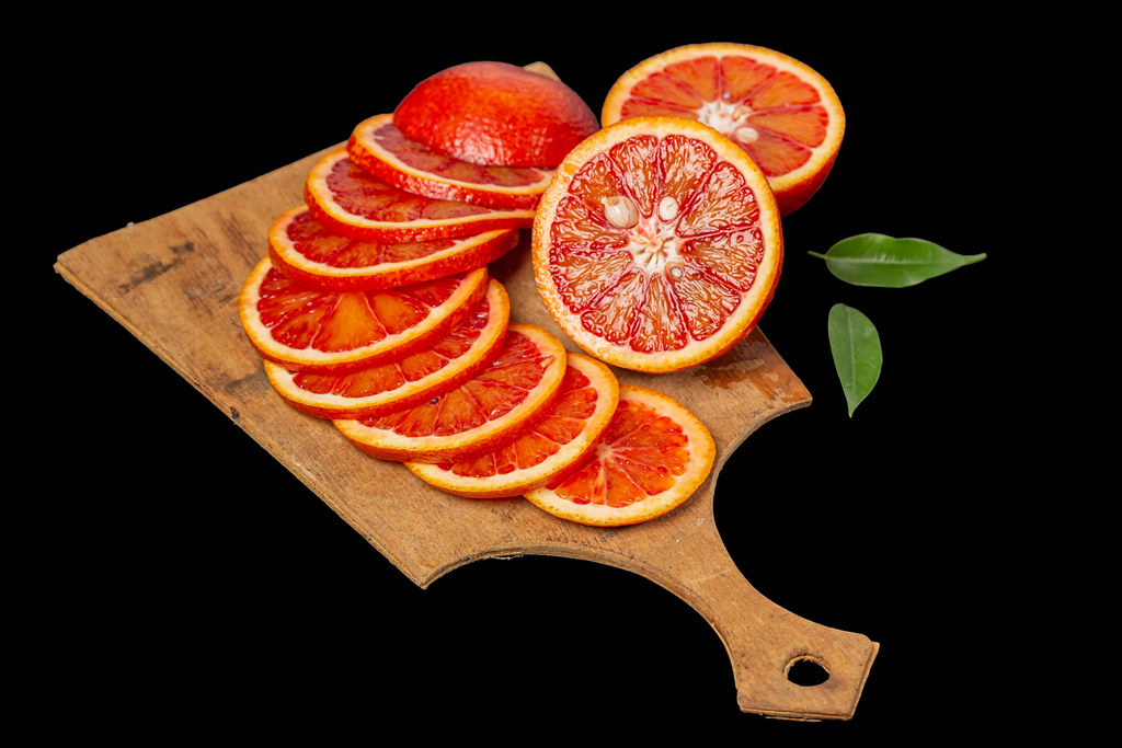 Sliced ripe sicilian red orange on board, black background