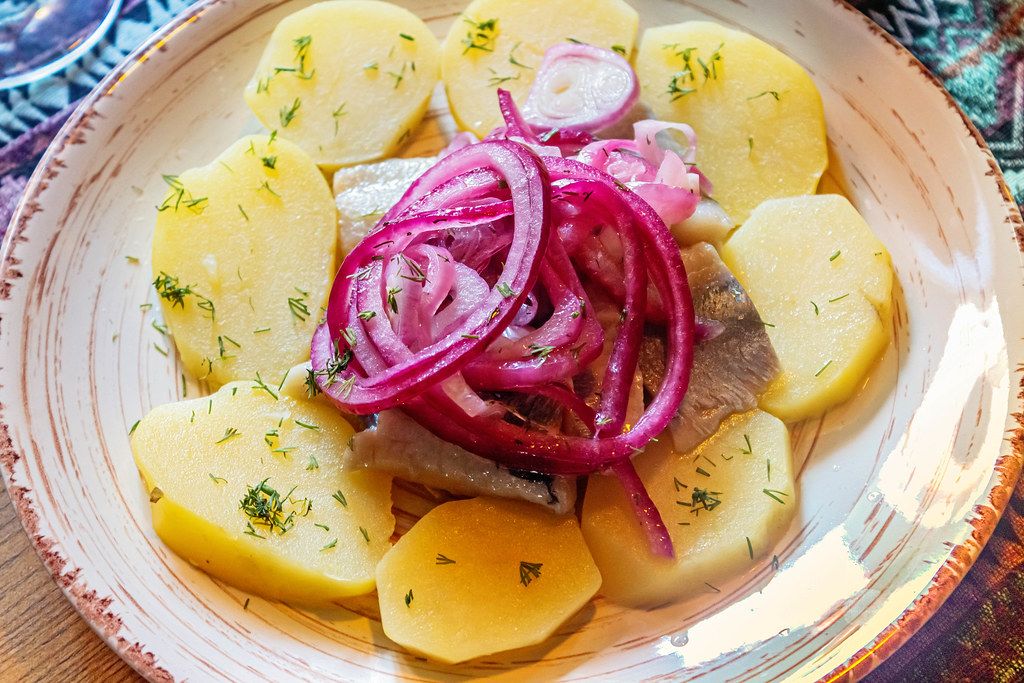 Slices of boiled potatoes and herring with pickled red onion