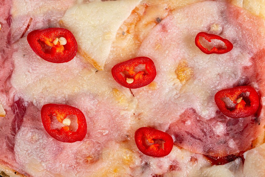 Slices of red hot chili pepper on a pizza with ham and cheese, close-up