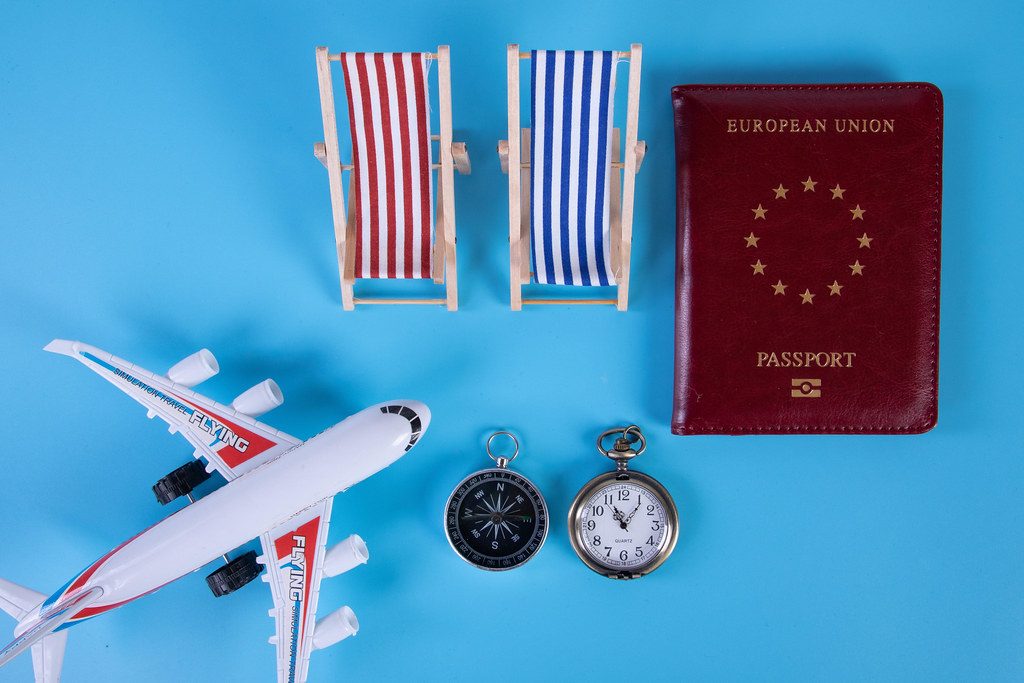 Small airplane, passport and beach chairs on blue background