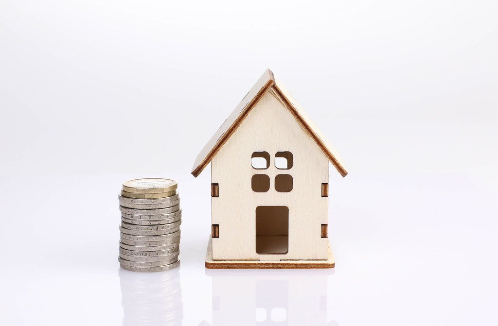 Small wooden house with coin stack on white background