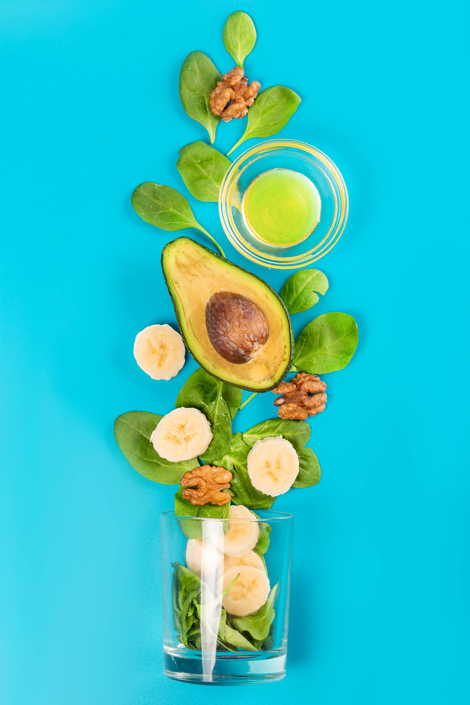 Smoothie ingredients - spinach, avocado, honey, banana and walnuts on a blue background