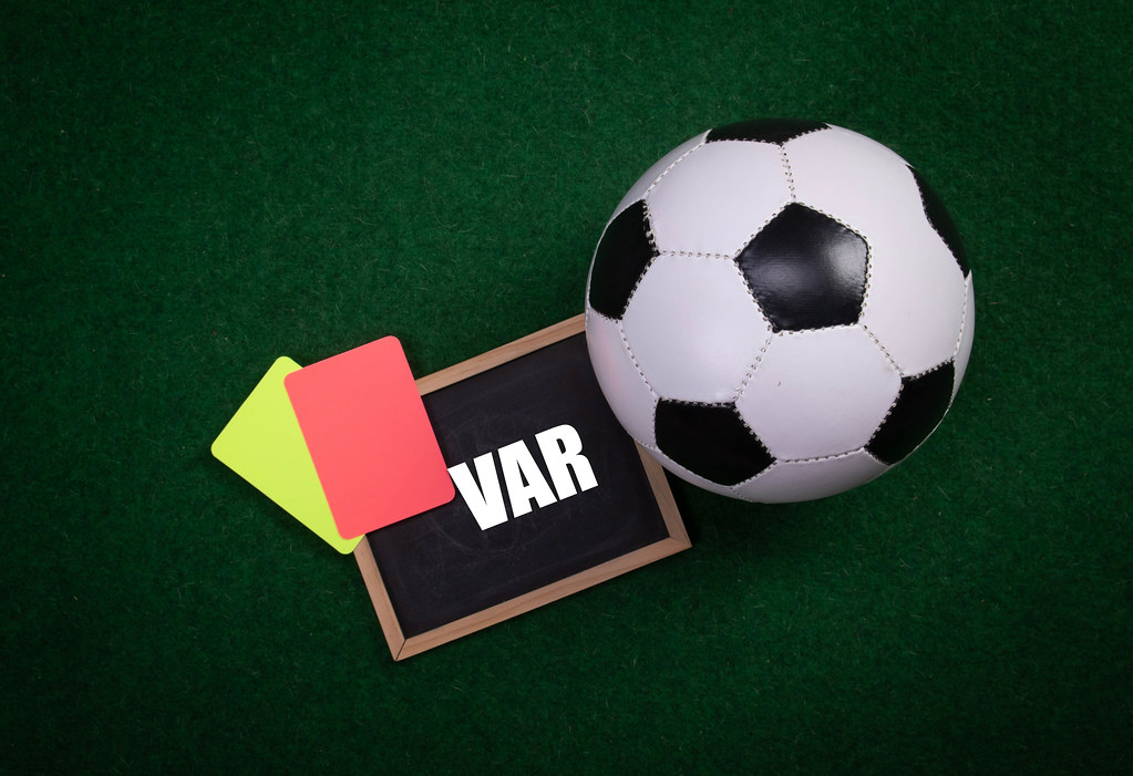 Soccer ball, referee cards and chalkboard with VAR text on a green grass