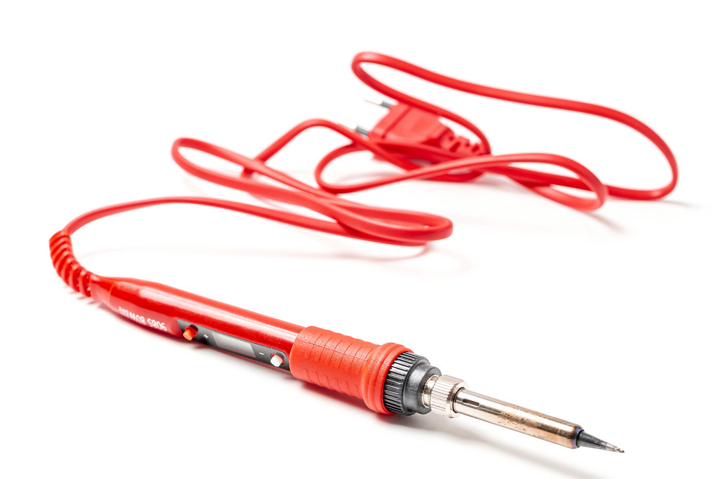 Soldering iron with red handle and cord on white background