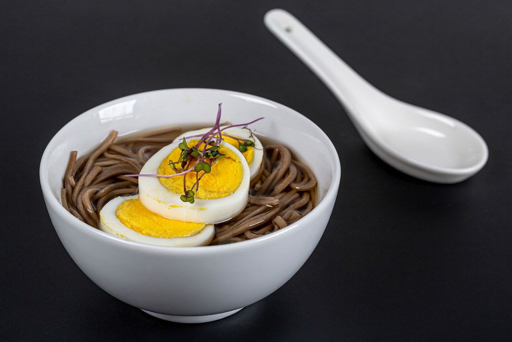 Soup with buckwheat noodles and boiled egg on a black background. Chinese food