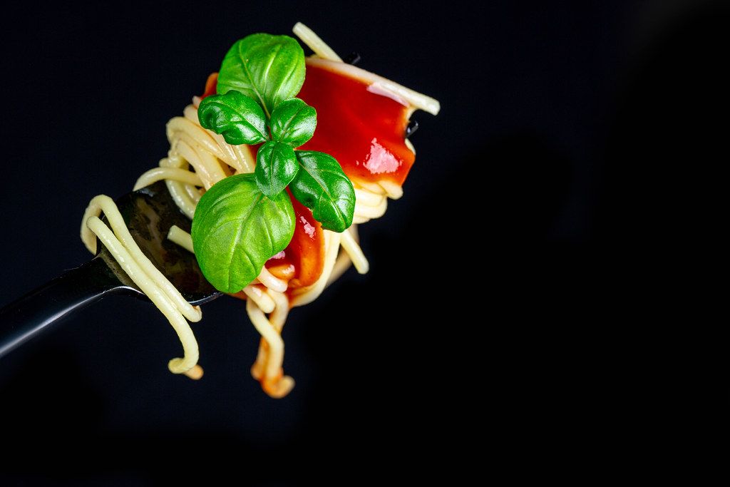 Spaghetti wound on a fork with red sauce and basil leaves on a black background