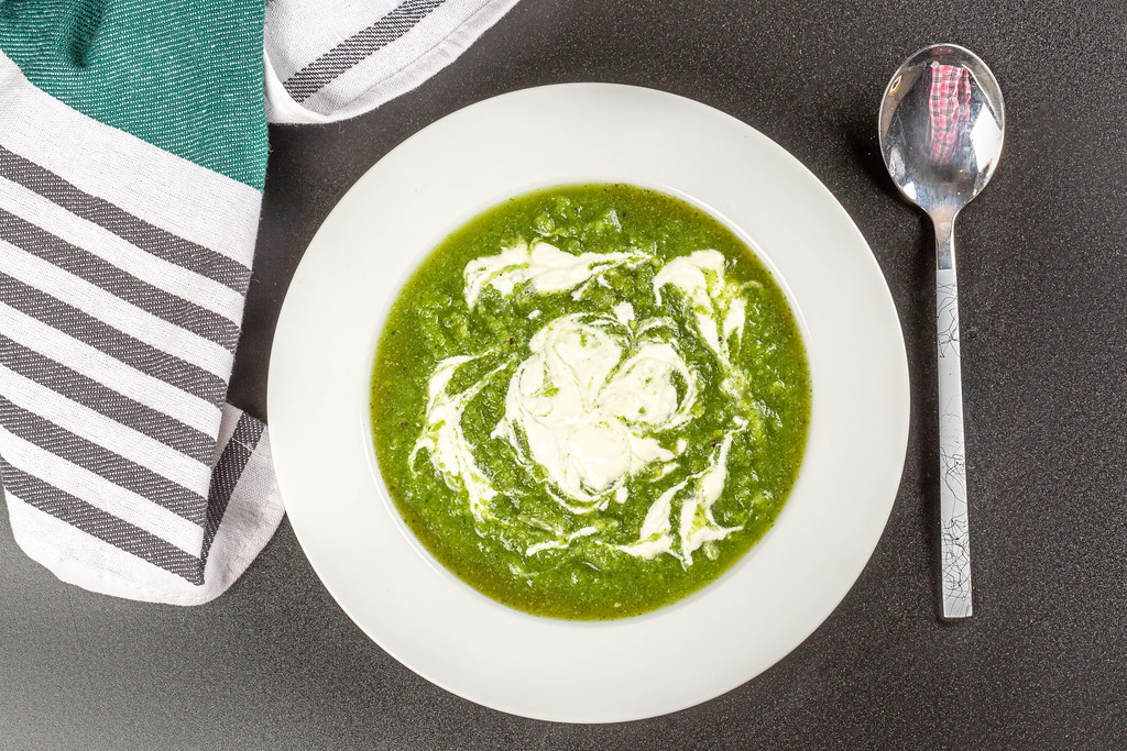 Spinach soup with cream in a bowl, top view