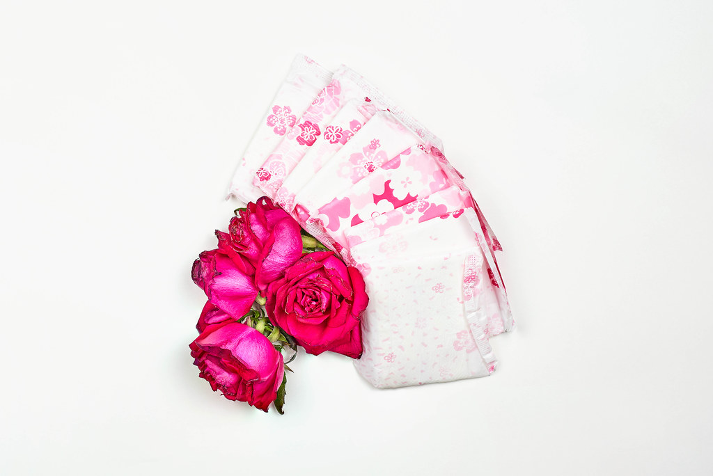 Stack of menstrual pads with red rose on white background