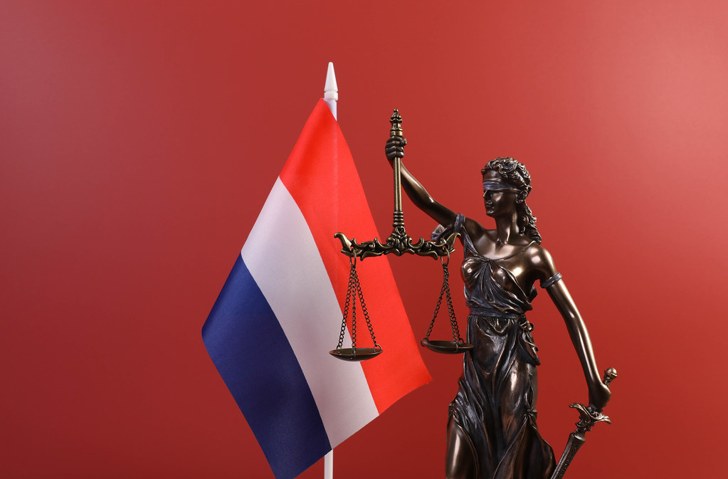 Statue of Lady Justice and flag of Netherlands on red background