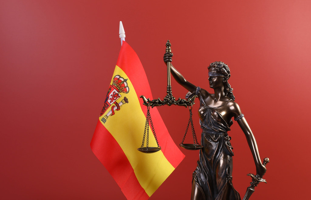 Statue of Lady Justice and flag of Spain on red background