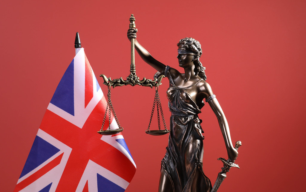 Statue of Lady Justice and flag of United Kingdom on red backgorund