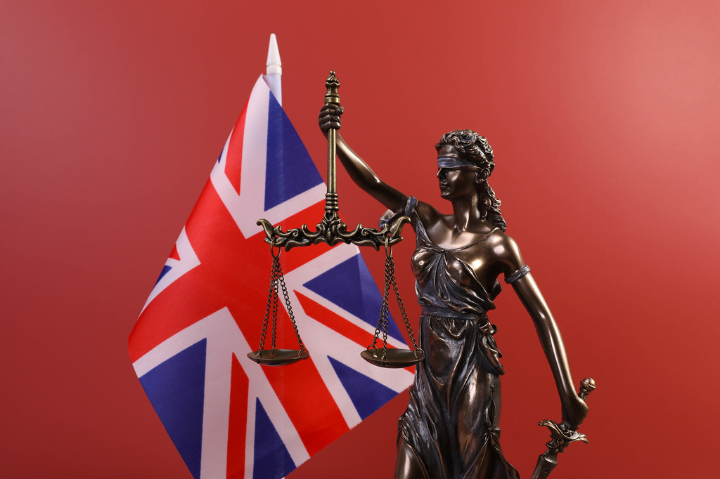 Statue of Lady Justice and flag of United Kingdom on red background